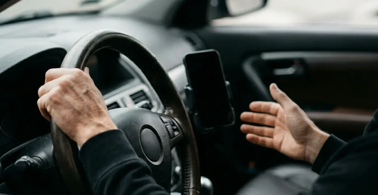 Main tenant un smartphone dans l'habitacle d'une voiture symbolisant les risques du téléphone au volant