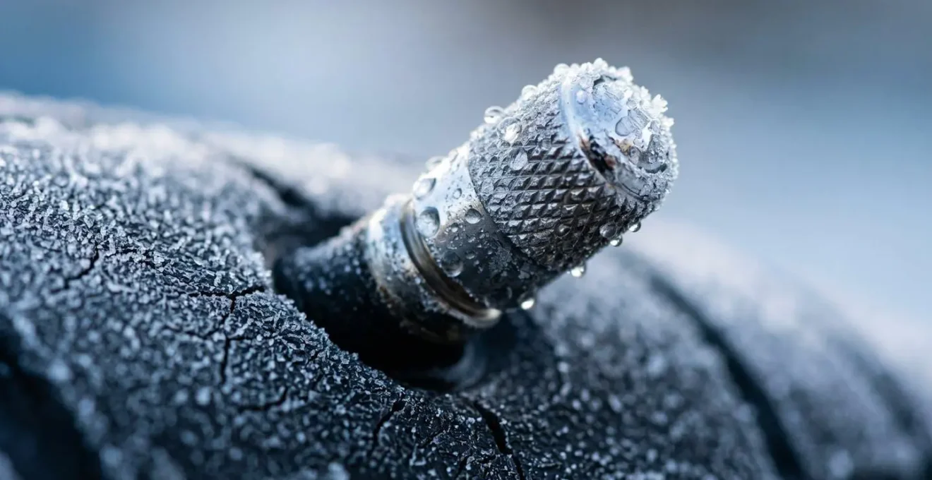 Détail macro d'une valve de pneu avec formation de givre et condensation illustrant l'impact du froid sur la pression
